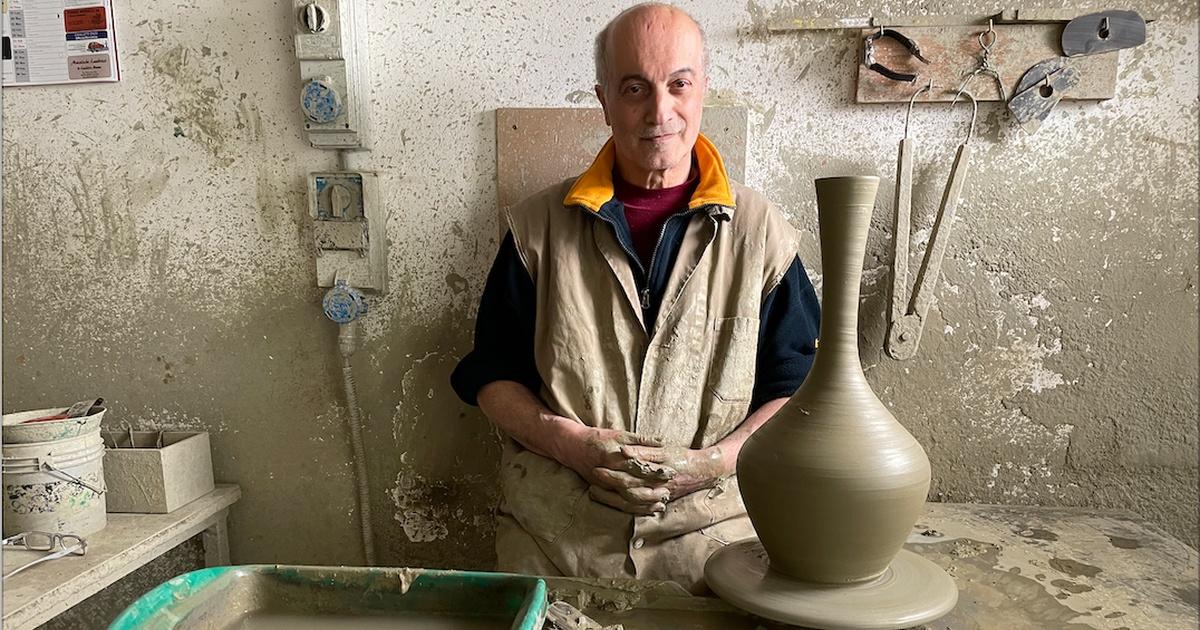 A white male standing next to a clay vase he has just created.