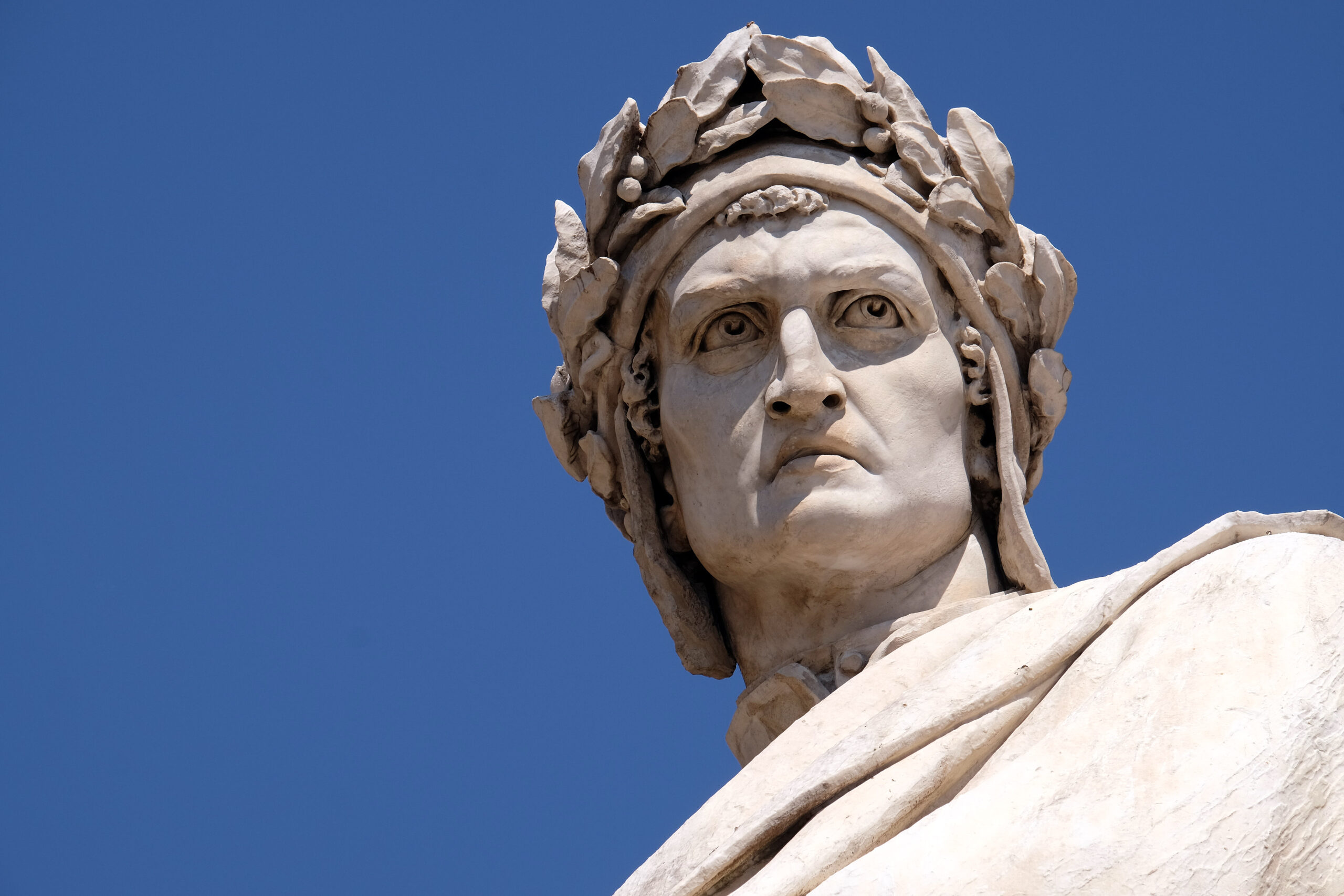 A statue of Dante Alighieri, the poet. It is an up close shot of his face with a blue sky backdrop.