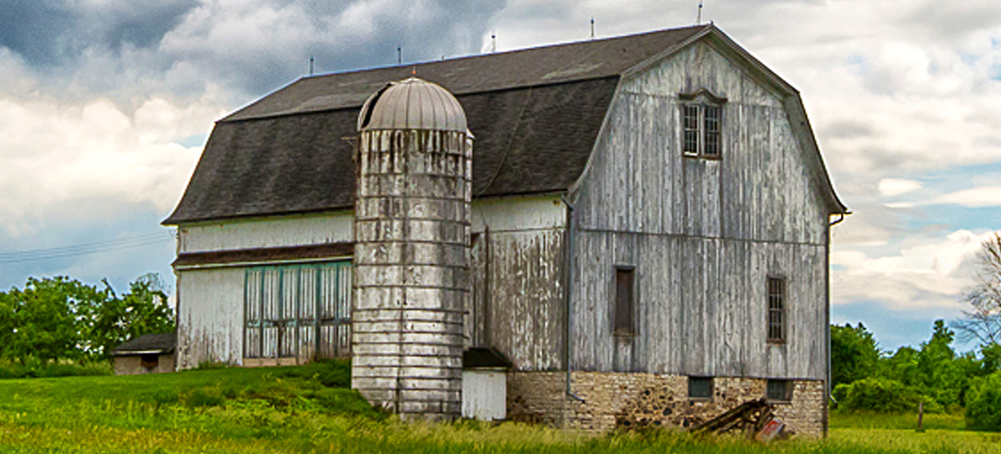 A white barn with a dark brown roof and a shite silo on a farm