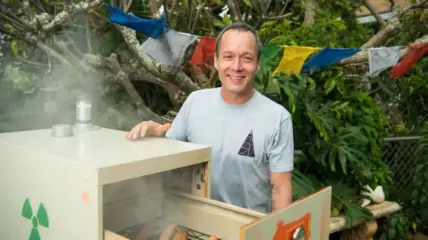 A white male with short dark hair wearing a light blue t-shirt stands behind a slow cooker