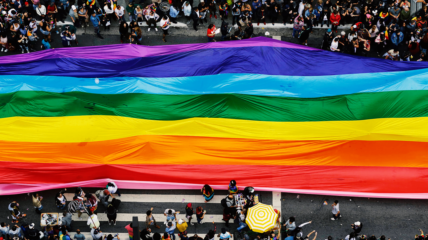 Overhead view of a PRIDE parade carrying a large rainbow flag covering the street