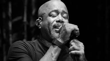 A Black man with a gray beard and mustache sings into a microphone