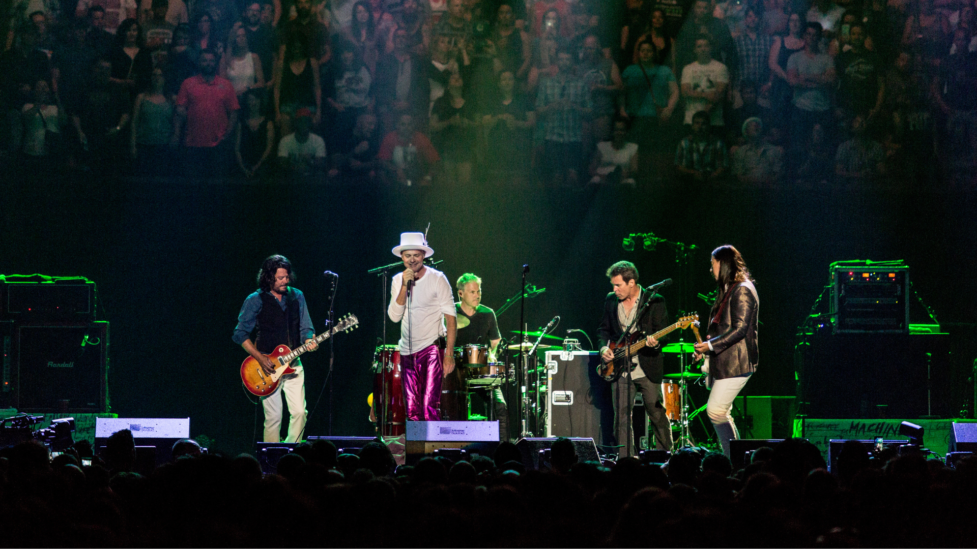 A band with five musicians stand on a stage performing