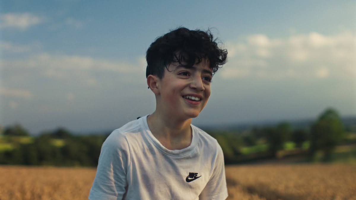 A white young boy with dark brown curly hair wearing a white t-shirt smiling