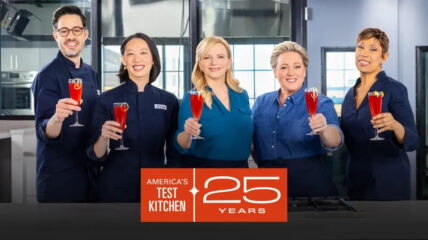 America's Test Kitchen crew holds up champagne glasses to toast their 25th anniversary.