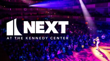 Logo for NEXT at Kennedy Center in white lays on top of an overview shot of a stage with a singer performing