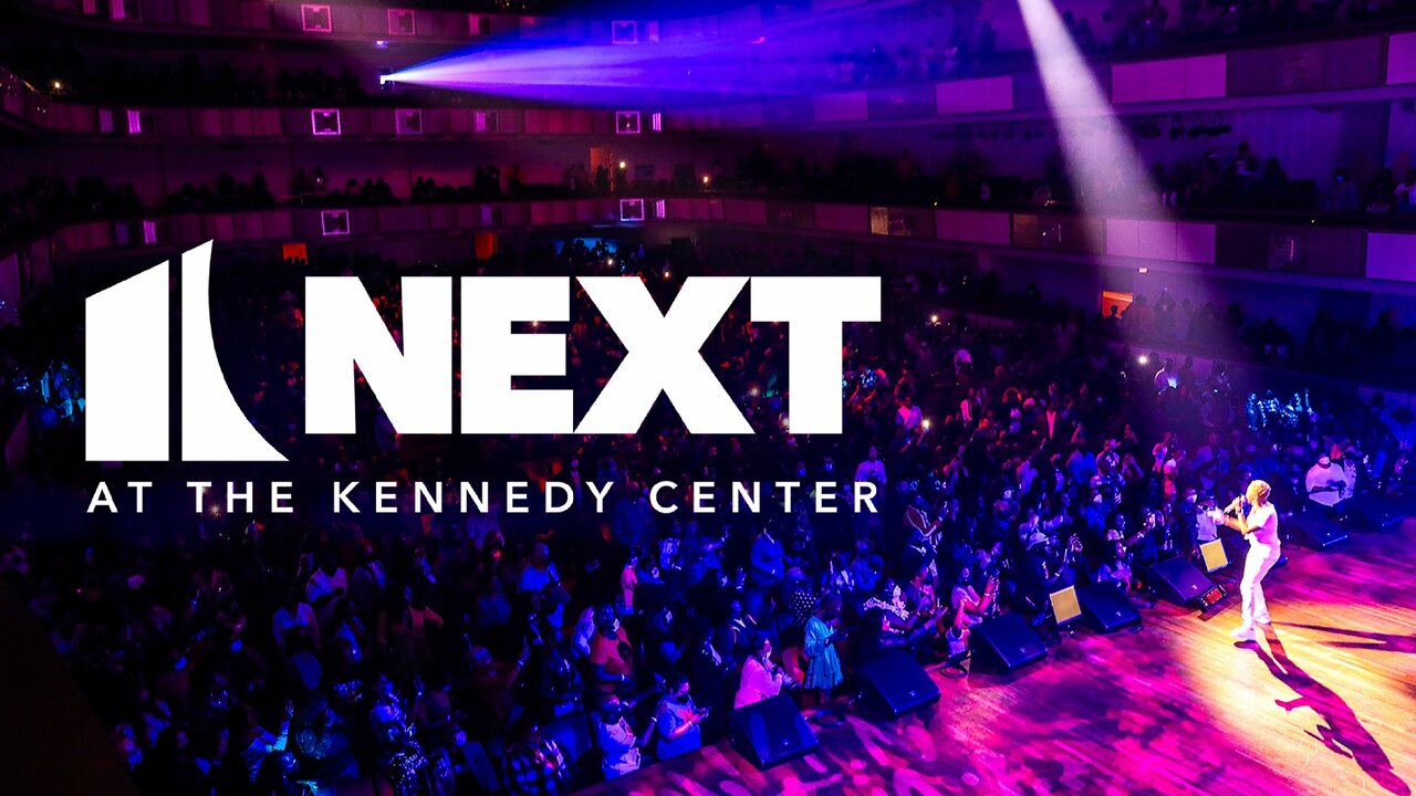 Logo for NEXT at Kennedy Center in white lays on top of an overview shot of a stage with a singer performing