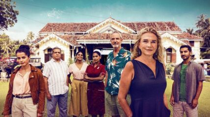 Eight cast of The Good Karma Hospital stand outside in front of a white cottage hospital.