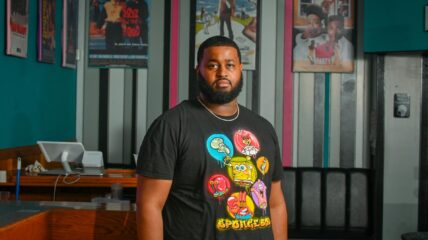 A Black Man with a beard wearing a t-shirt looks out at the camera