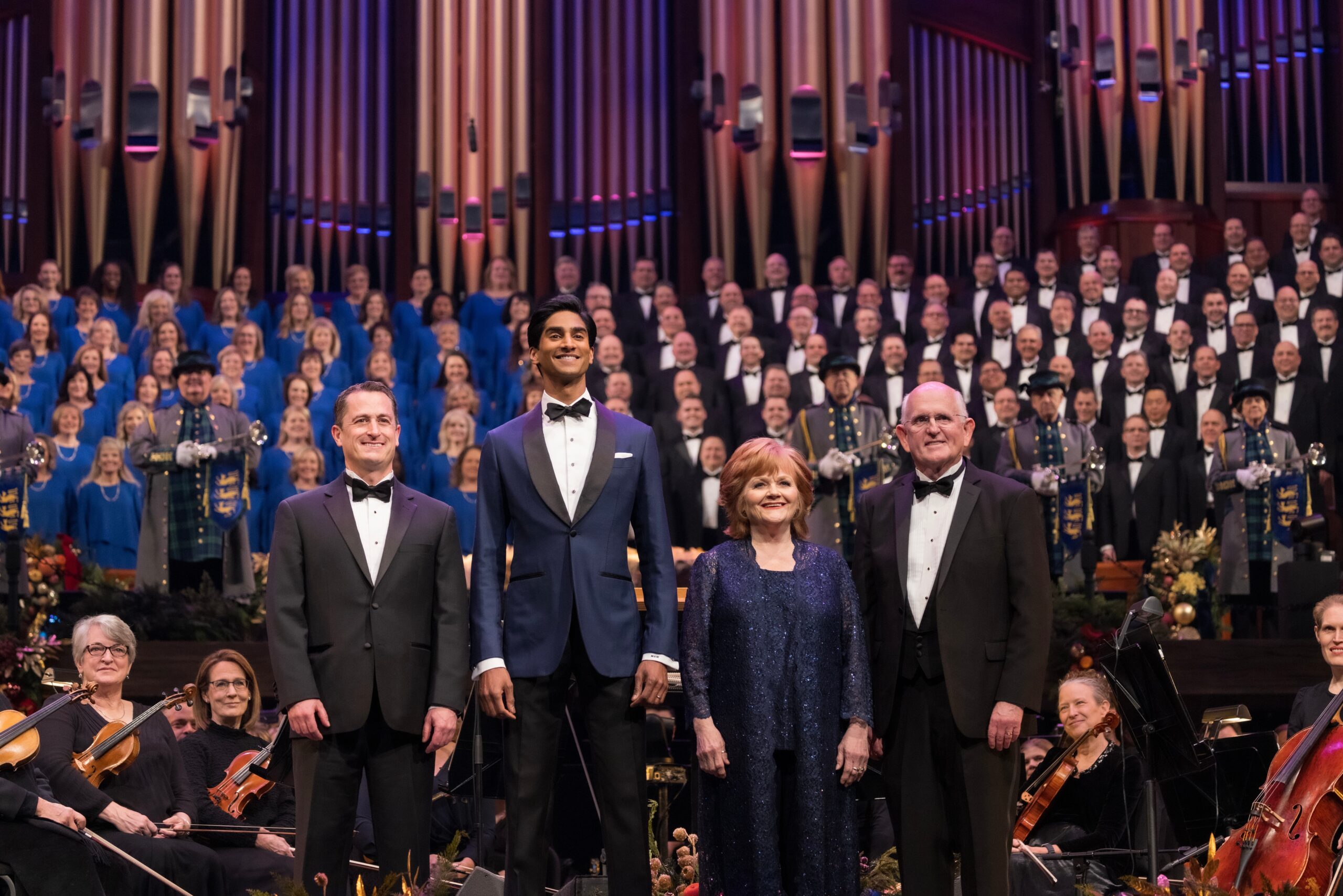 Performers Ryan Murphy, Michael Maliakel, Lesley Nicol, and Mack Wilberg stand on stage with the Tabernacle Choir in the background