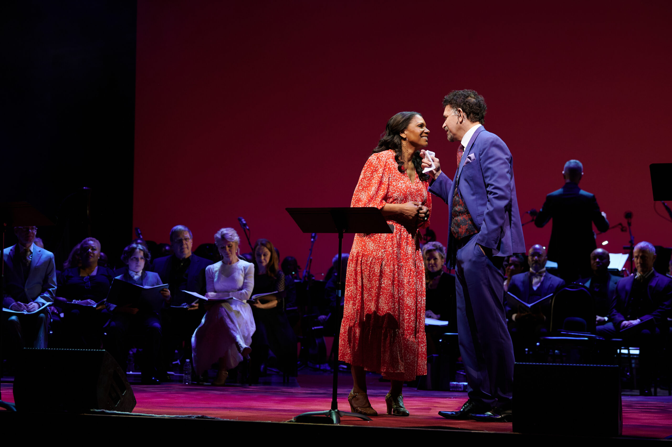 Audra McDonald wearing a red dress looks at Brian Stokes Mitchell, who wears a blue suit. He has his hand holding her chin.