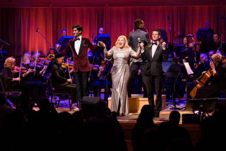 Michael Maliakel, Megan Hilty, and Luke Hawkins stand on a stage holding hands.