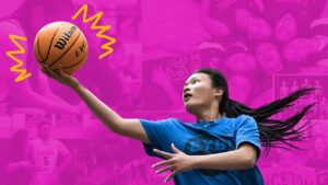 A girl with long Black hair pulled back in a pony tail wearing a blue t-shirt with a basket ball in her hand about to do a lay up.