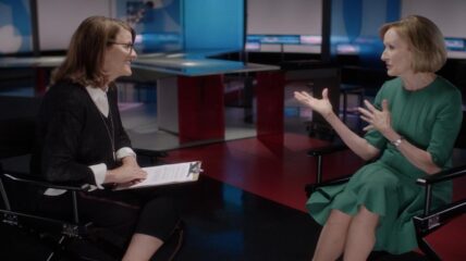 Kelly Corrigan wearing a Black sweater and white blouse sits across from Judy Woodruff, who is wearing a green dress