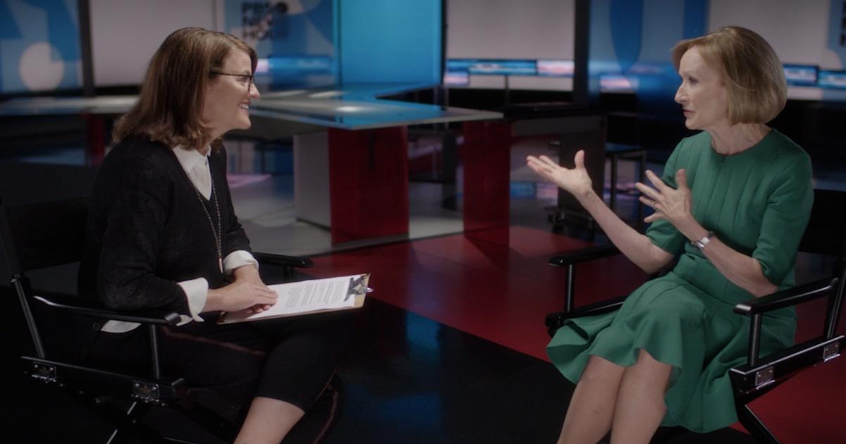 Kelly Corrigan wearing a Black sweater and white blouse sits across from Judy Woodruff, who is wearing a green dress