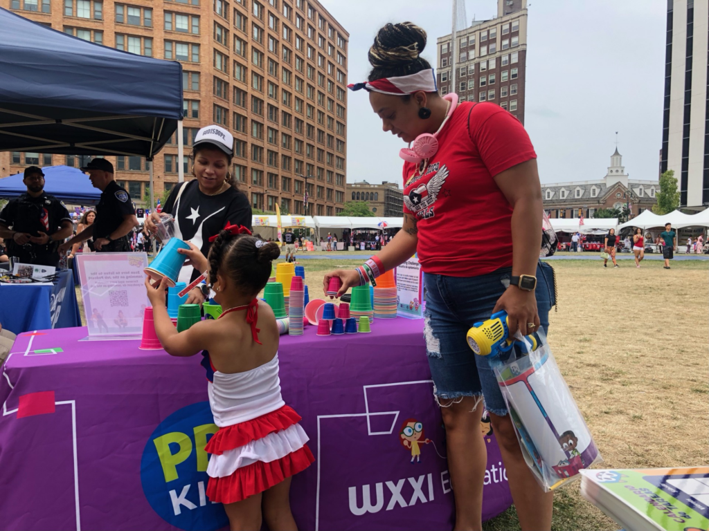 Mon and daughter standing in front of the PBS KIDS table playing an activity.