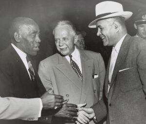 Three men stand together shaking hands.