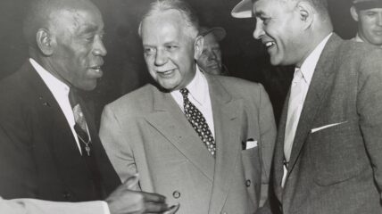 Three men stand together shaking hands.