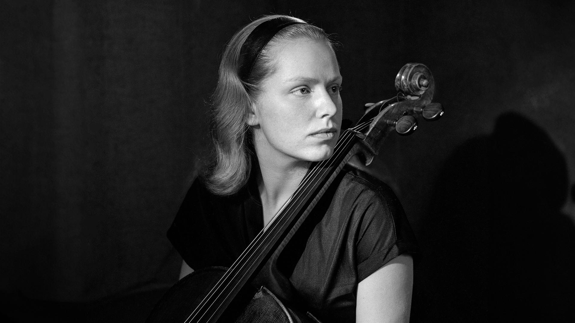 A young Jacqueline Mary du Pré , cellist. She's wearing a dark dress with a dark headband pulling her hair back